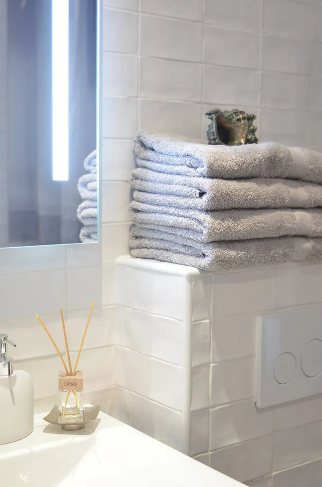 Stacked towels and a reed diffuser beside a tiled sink