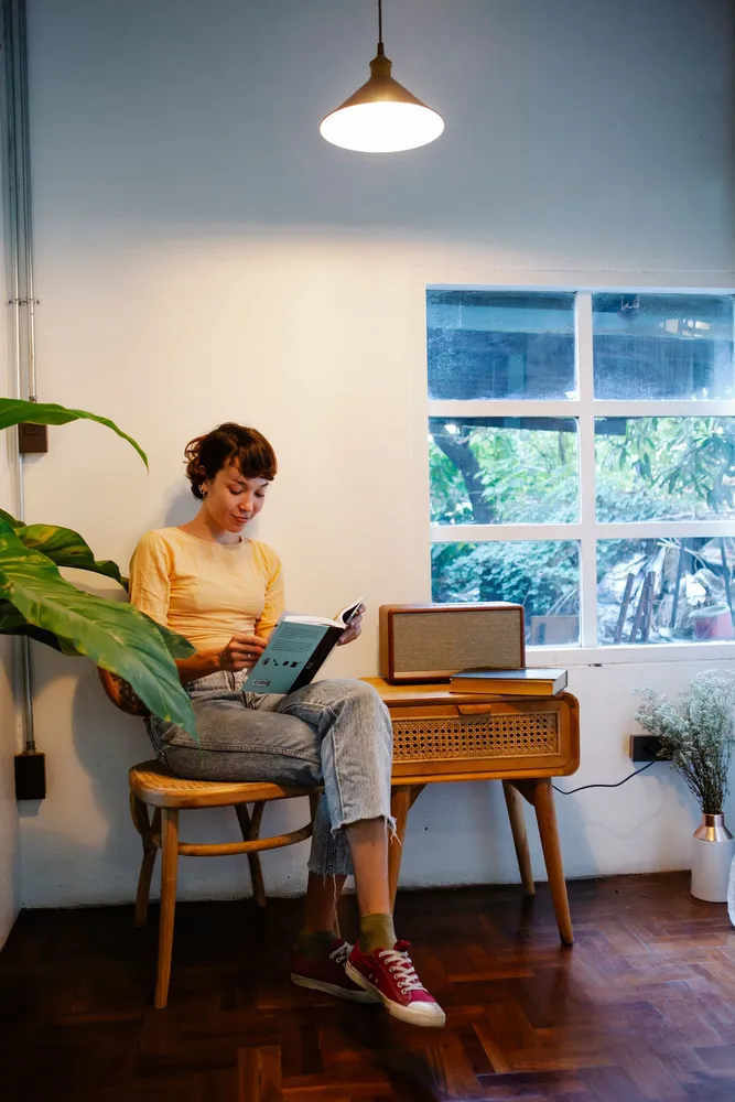 Person reading a book in a chair beside a floor lamp